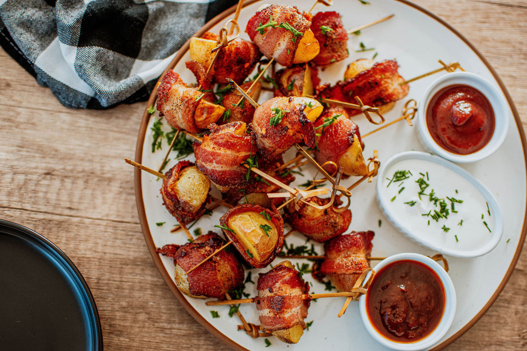 bacon wrapped potato bites on a plate with dipping sauces