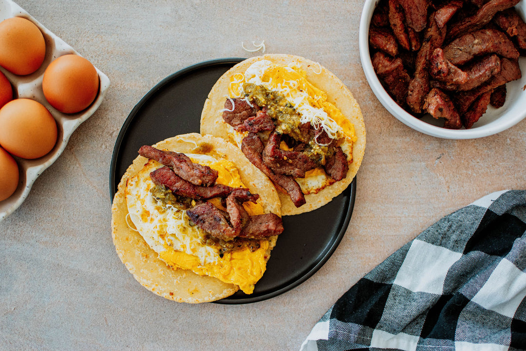 breakfast tacos with eggs, steak, cheese, and green salsa on a plate