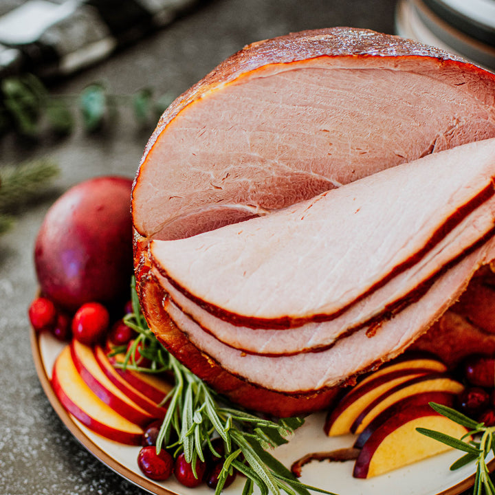 organic bone in half ham on a platter with apples, rosemary, and cranberries